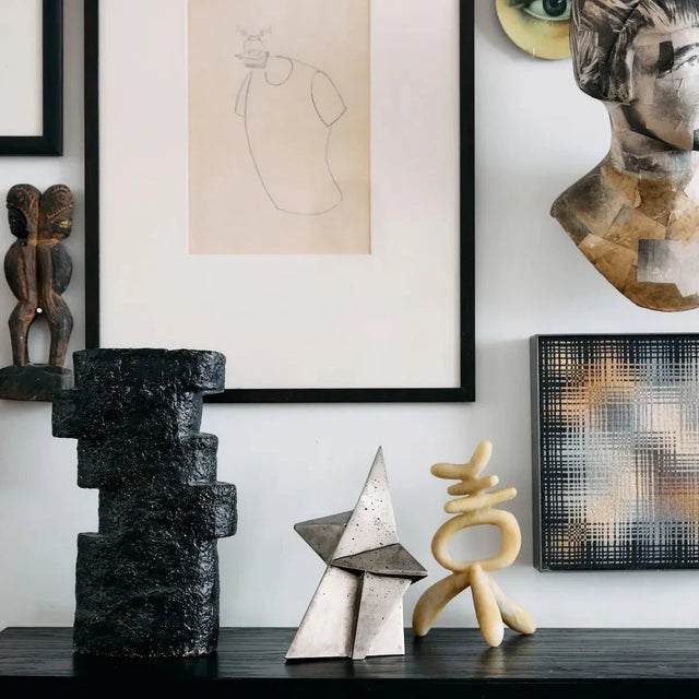 Schwarzes Sideboard mit drei Skulpturen vor Bilderwand mit Zeichnung und Kunstobjekten – moderne Wohnzimmer Deko