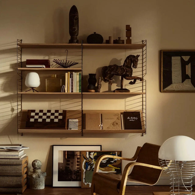 String Regalsystem Vorteilsset als Wandregal mit Eichenböden, dekoriert mit Büchern, Lampe und Skulpturen neben einem Sessel
